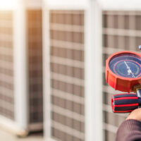 Air repair mechanic using measuring equipment for filling industrial factory air conditioners and checking maintenance outdoor air compressor unit.